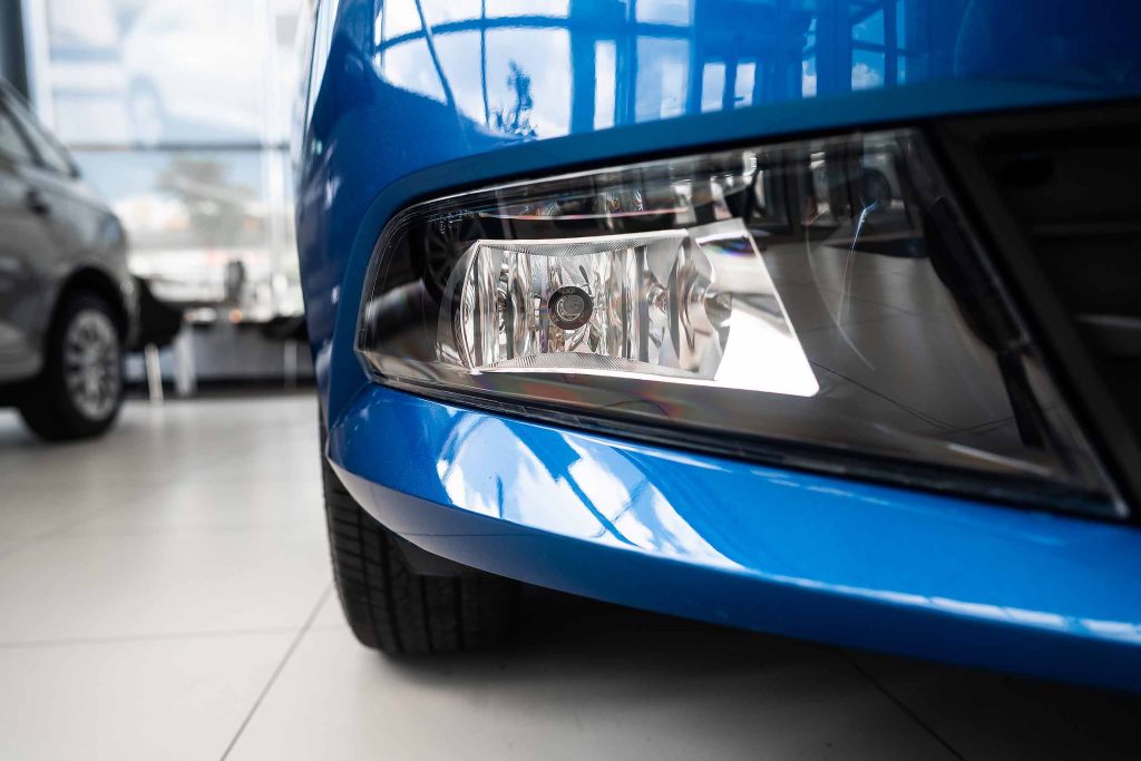 Close-up of a blue car's headlight and front bumper in a showroom.