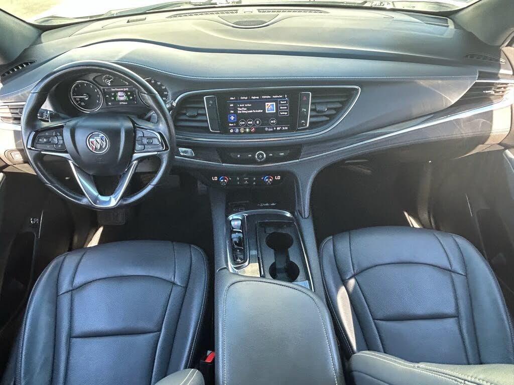 13 Front interior of a Buick vehicle featuring a leather-wrapped steering wheel, large touchscreen dashboard, and black leather seats.