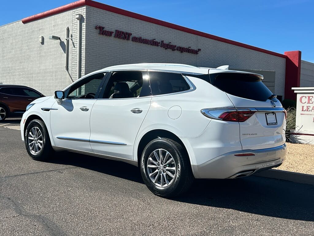 3 A white SUV parked in a lot beside a beige commercial building with a red trim under a blue sky.