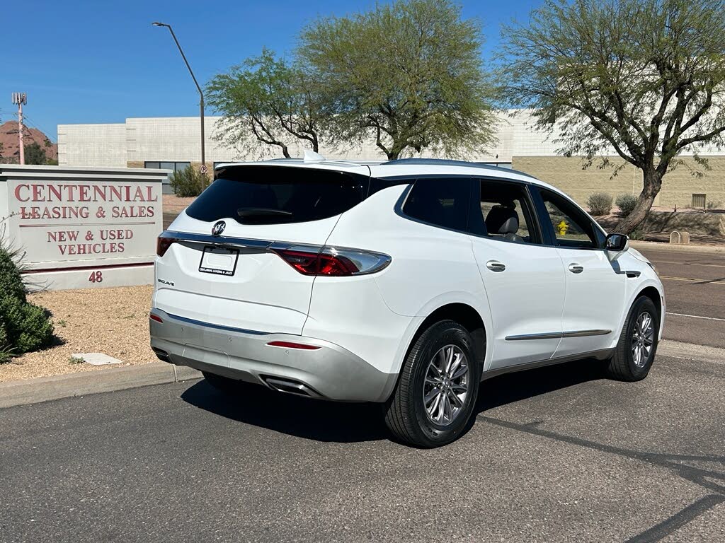 5 White SUV parked on a street beside a dealership sign with trees and blue sky in the background.