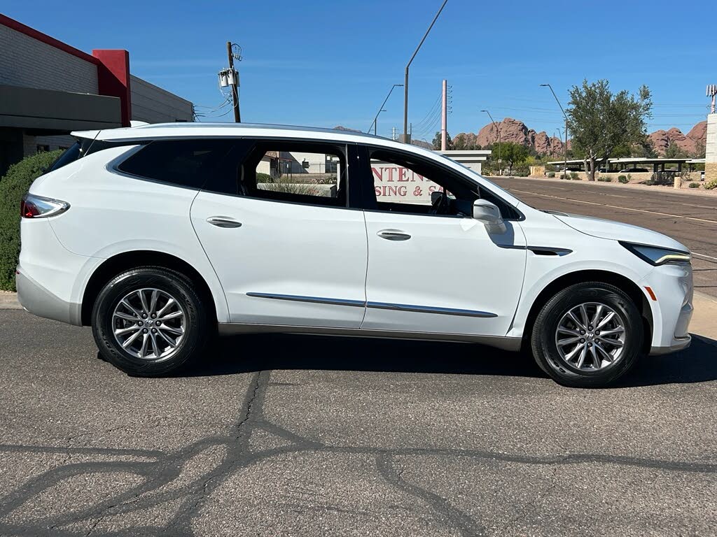6 Side view of a white SUV parked on a paved lot with a red-roofed building and desert hills in the background.
